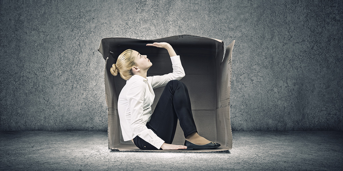 Woman sitting in cardboard box in concrete room