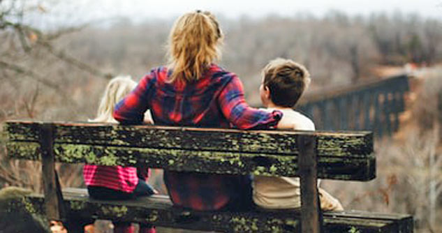Mom, 2 kids, backs to us, sit on bench in nature
