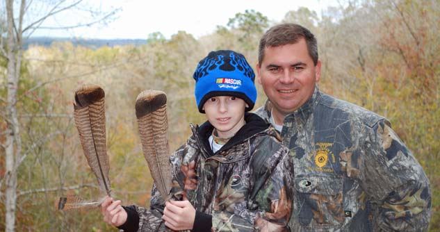 Boy holds feathers, dressed in cammo alongside Catch a Dream host