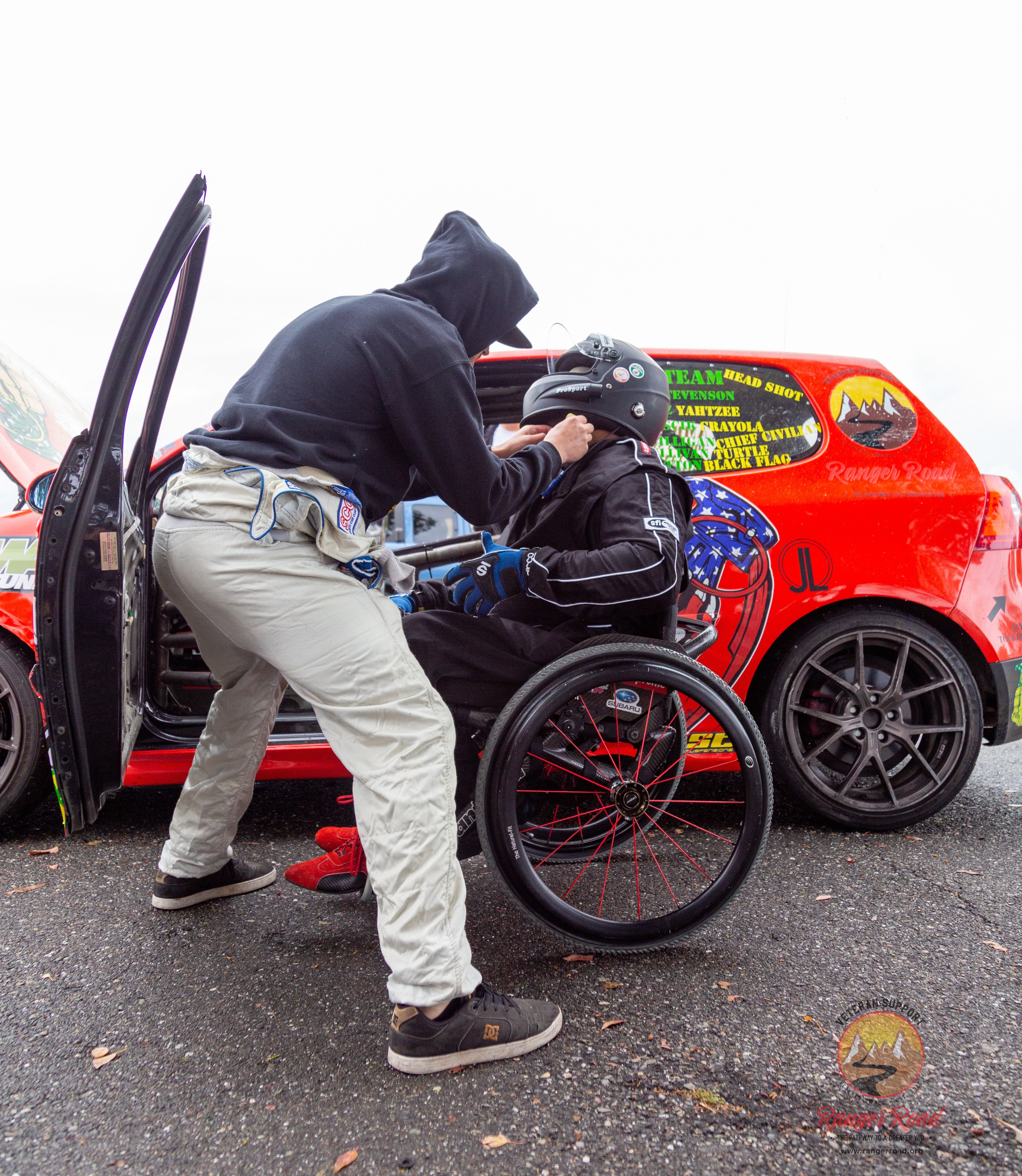 Man in wheelchair gets help with his helmet to drive racecar