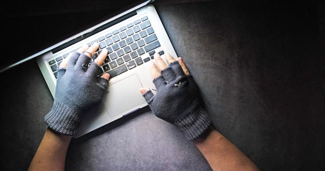 Man wearing gloves taps on keyboard in near dark