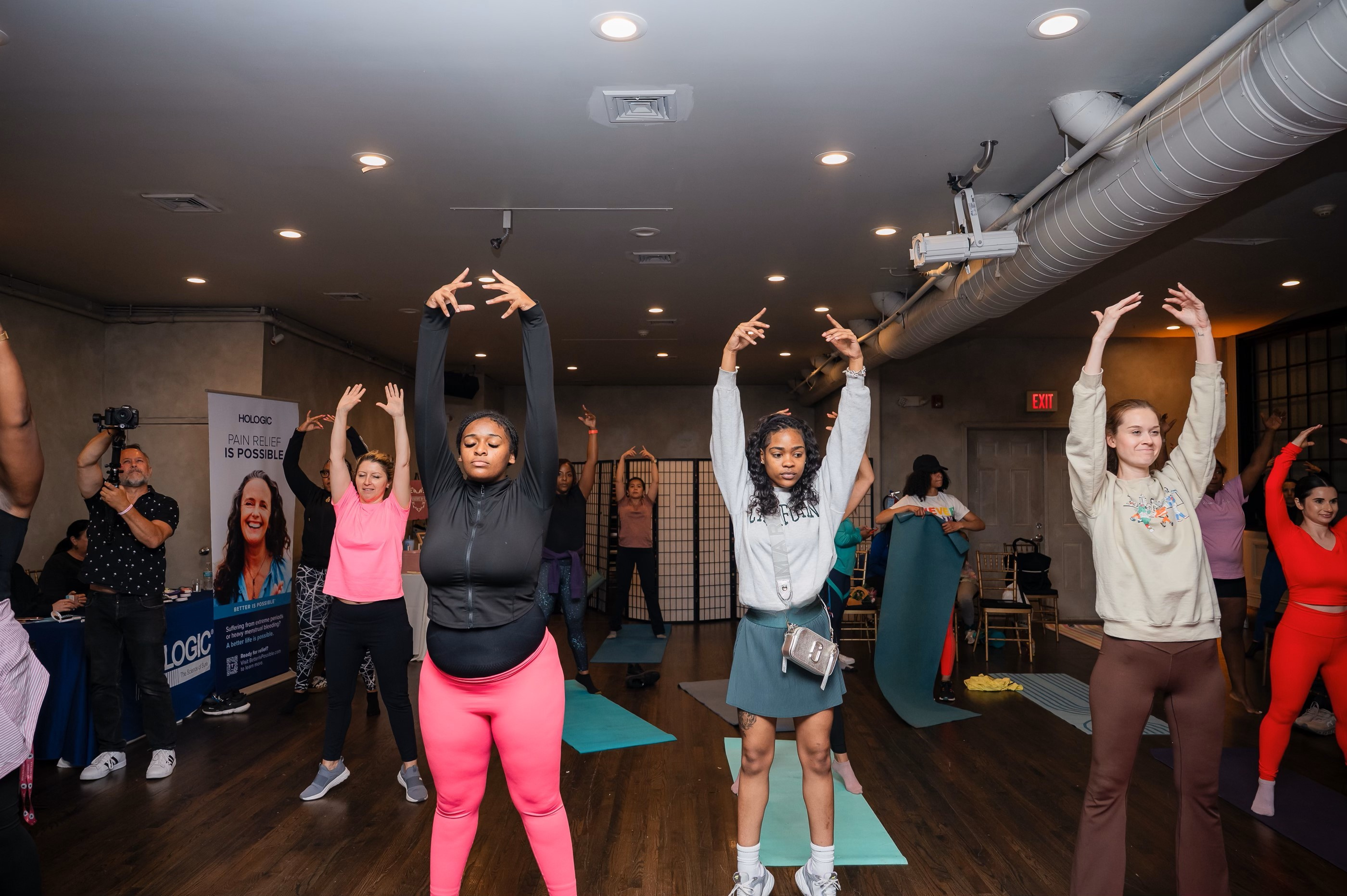 11 people in a room with their hands in the air as they work on a yoga pose, practicing breathing,
