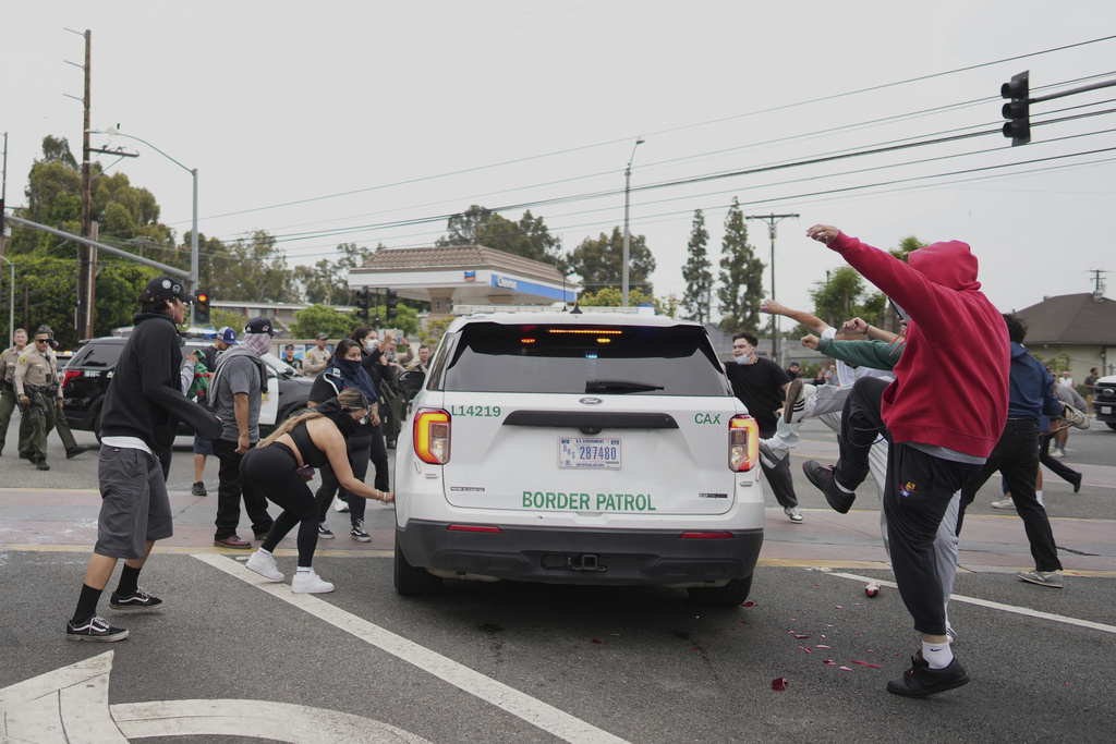 Protesters kick the side of a Border Patrol vehicle during a demonstration over the dozens detained in an operation by federal immigration authorities