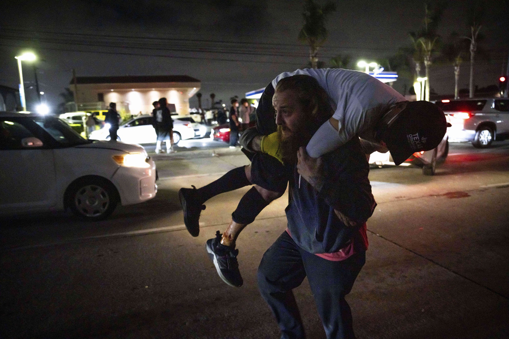A person carries an injured protester to cover during a protest in Compton, Calif.
