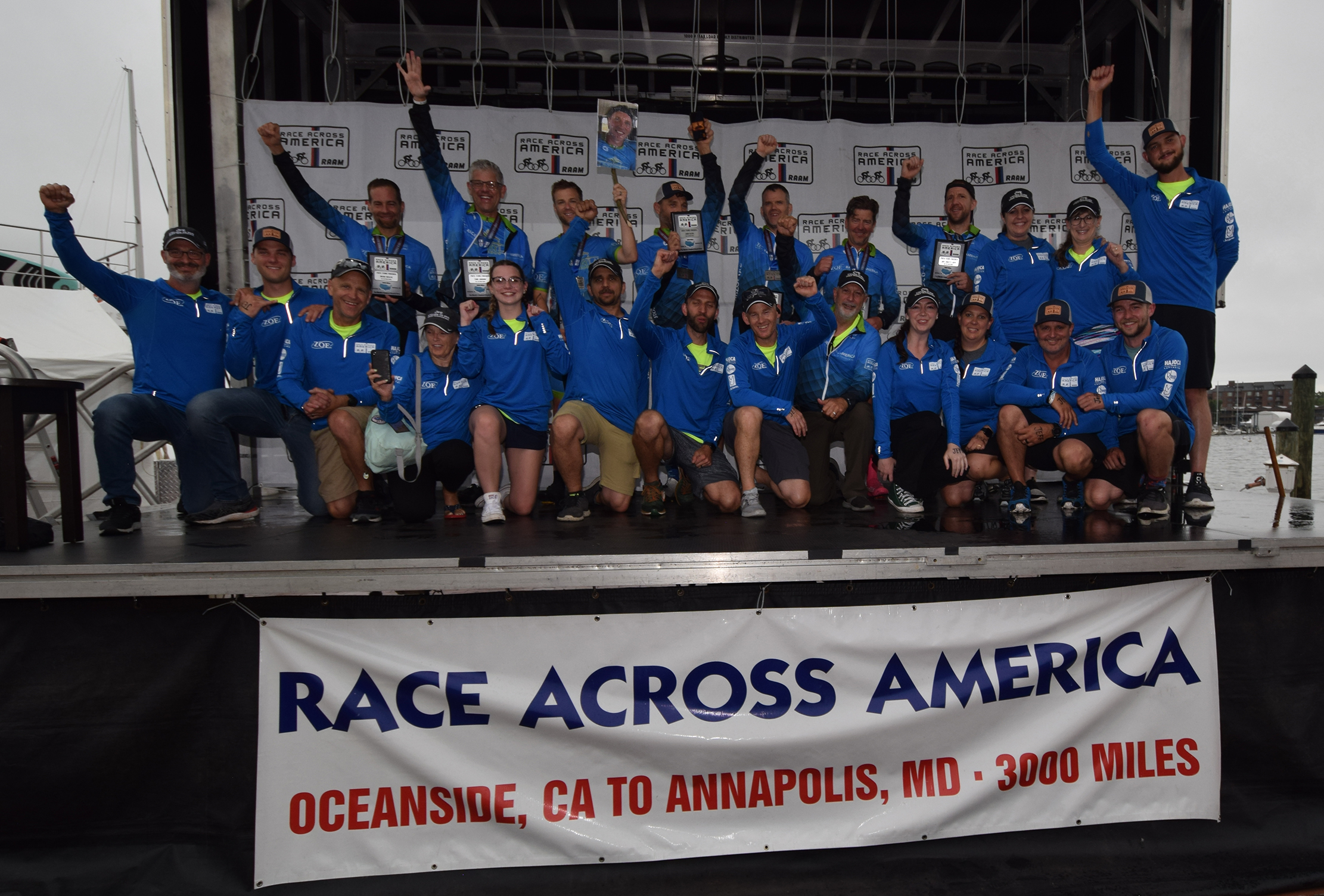 24 members of the ZOE international team and crew raise their hands as they celebrate standing on the Race Across America finish line.