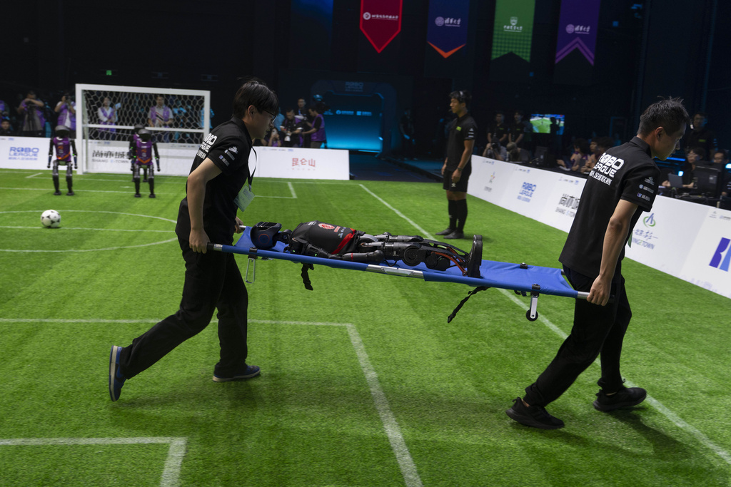 Workers carry out a T1 robot from Booster Robotics during the inaugural RoBoLeague robot soccer competition