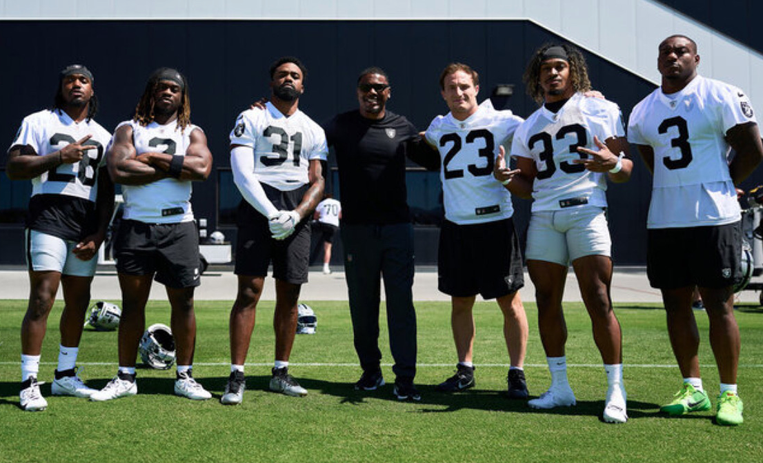 Man in black in the center flanked by 6 men in Raiders uniforms