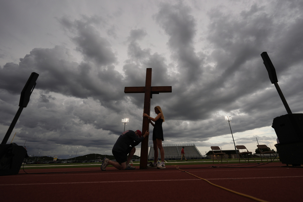 Dan Beazley, of Michigan, left, prays as he holds a large cross with Abigail Smithson during a vigil for flooding victims at Tivy Antler Stadium in Kerrville, Texas