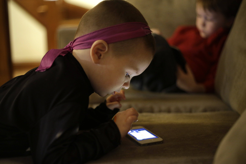 Nolan Young, 3, front, looks at a smartphone while his brother Jameson, right, 4, looks at a tablet in their home in Boston