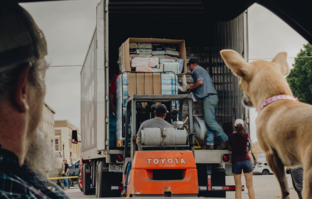 Man and small dog staring out car window and a Convoy big rig unloading supplies