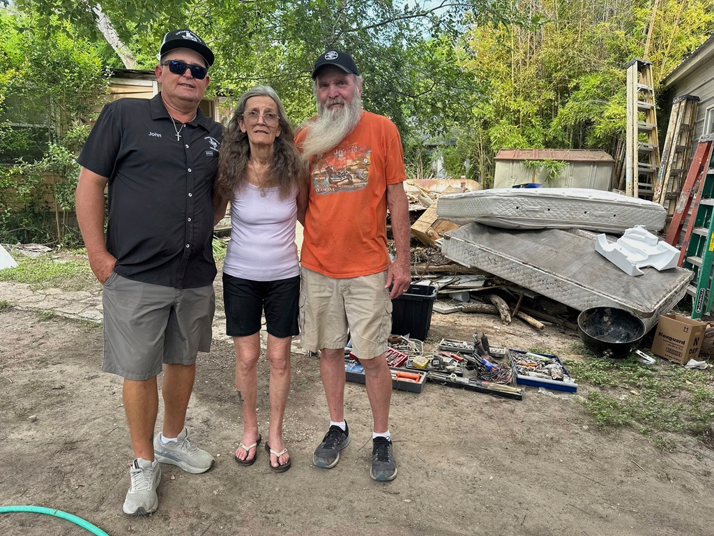 Colleen Lucas, center, and her husband, Dave, right, stand outside their flood-destroyed home in Ingram, Texas, with Lucas