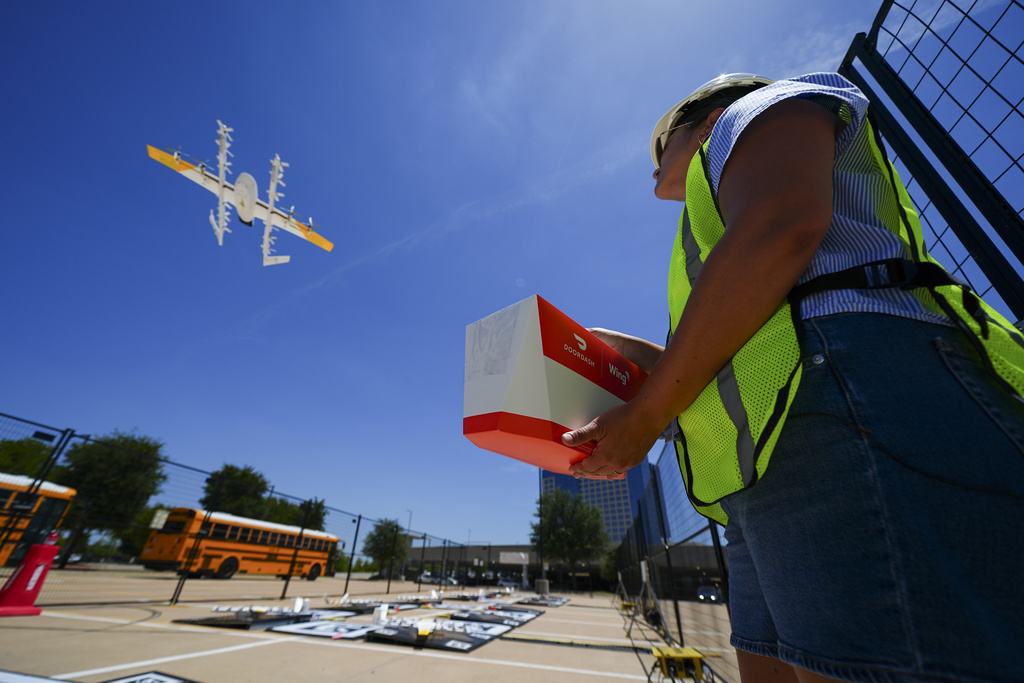Masslie Arias, of DoorDash, prepares to load a delivery package on a hovering drone 