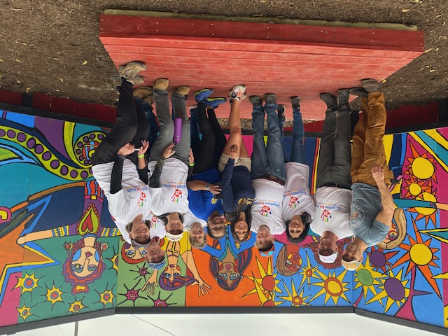 10 volunteers stand proudly in front of their recently completed mural on a stage.