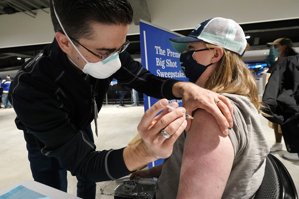 Seattle Kraken fan Jami Lopez, right, of Bellevue, Wash., receives a Moderna coronavirus booster vaccine from health care worker Zach Hren 