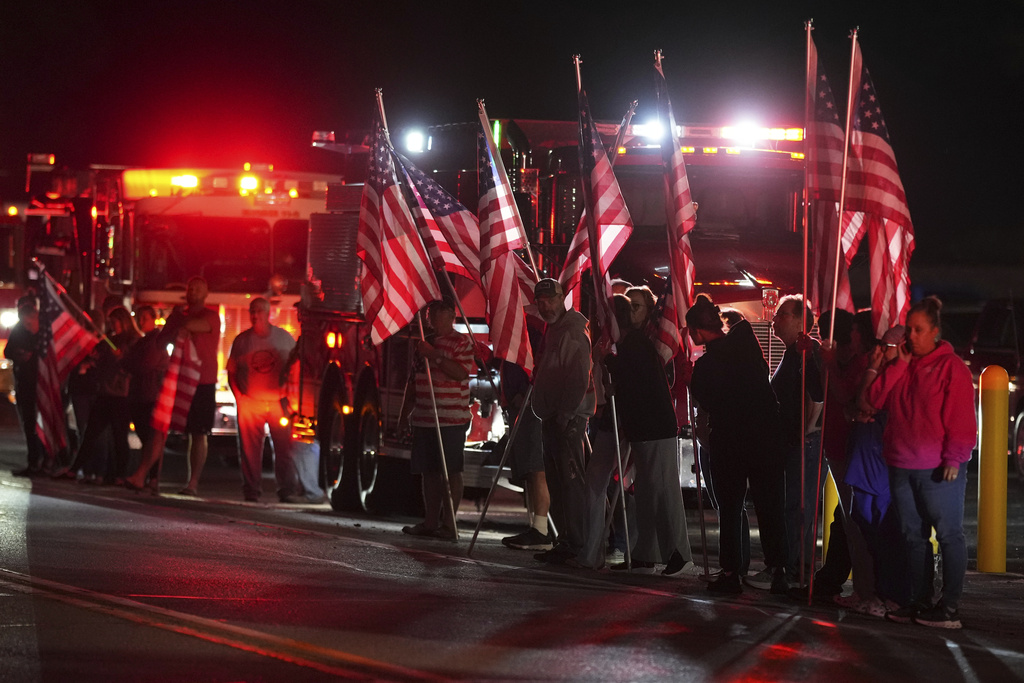 People hold American flags before a procession in Spring Grove, Pa., after multiple police officers were shot and killed. 