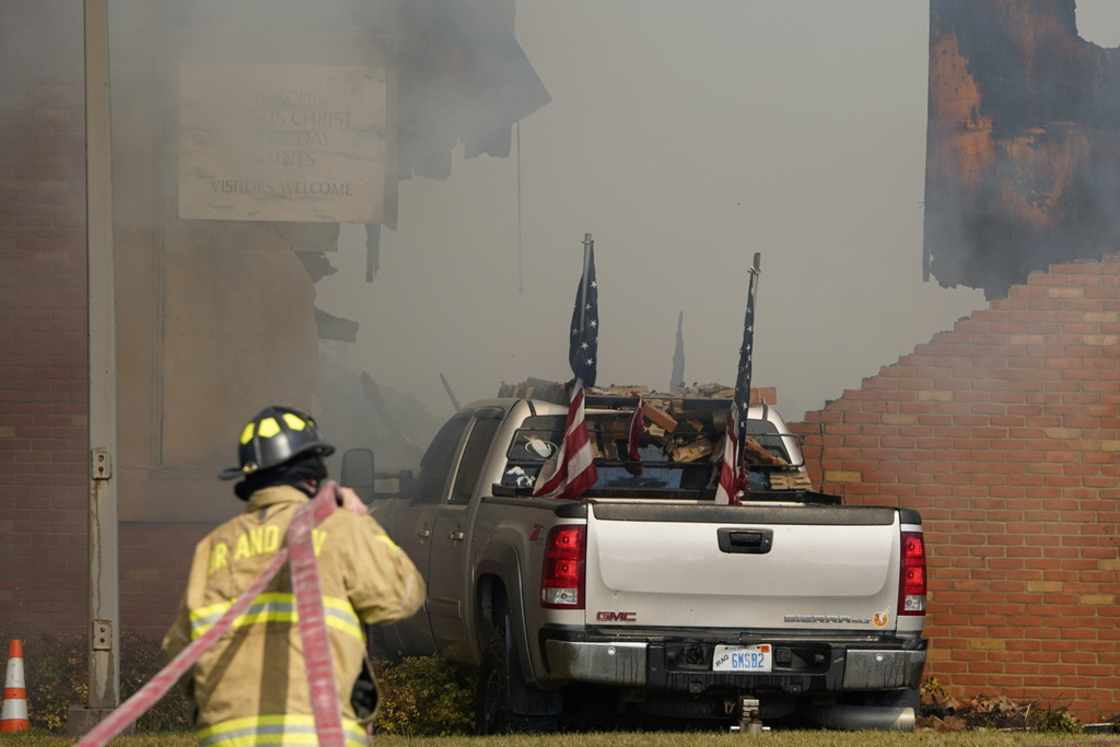 A vehicle that was rammed into the building is surrounded by smoke as a firefighter works on the scene at the Church of Jesus Christ of Latter-day Saints in Grand Blanc, Mich.