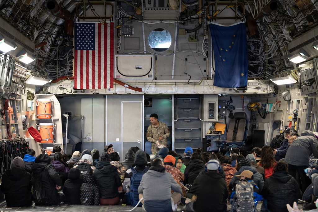 Alaska Air National Guard Staff Sgt. Angel Reyes distributes hearing protection to passengers while evacuating Alaskans displaced in the aftermath of Typhoon Halong 