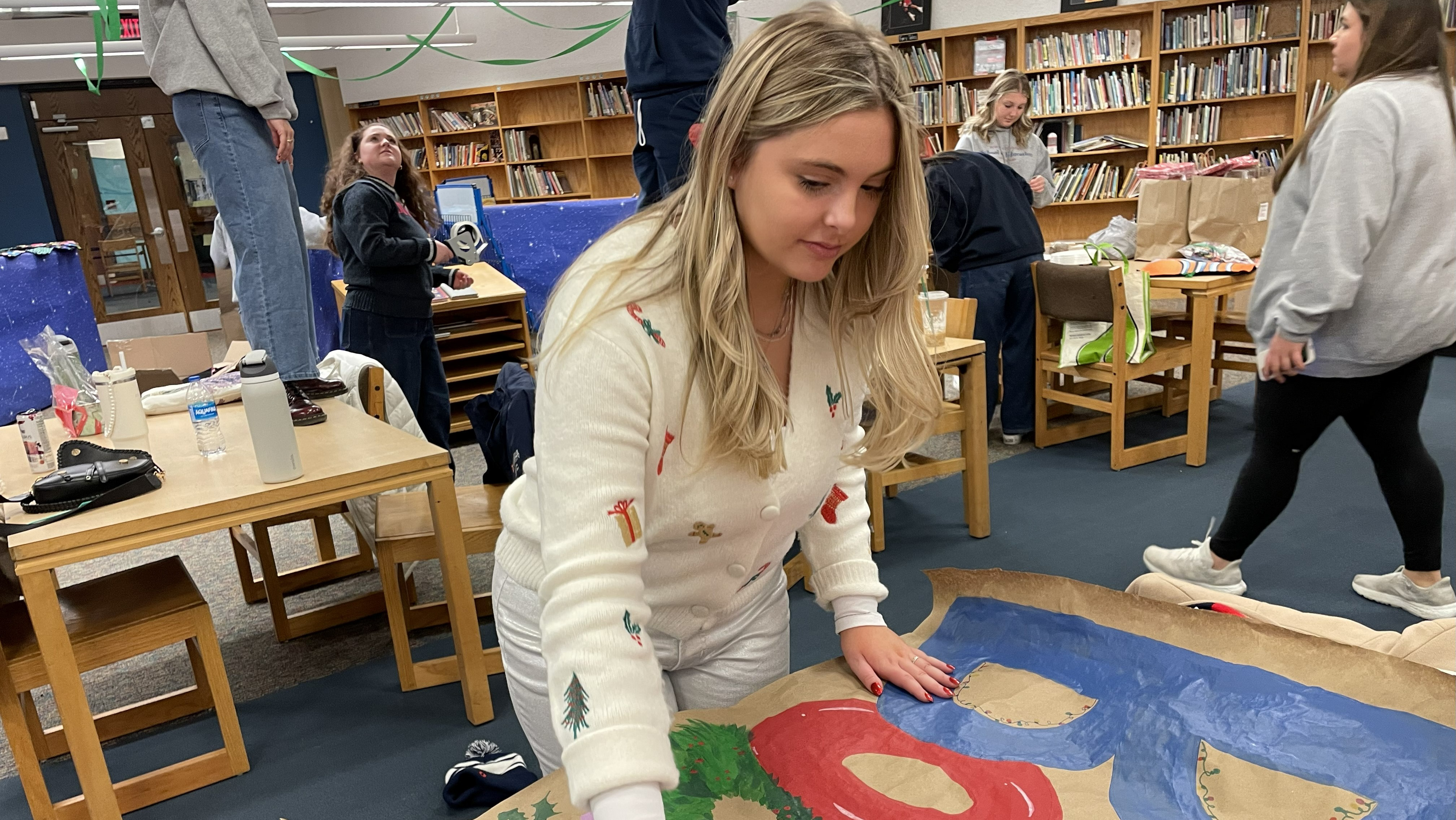 Zoe Burnick paints holiday sign as volunteers decorate the library for the celebration. 