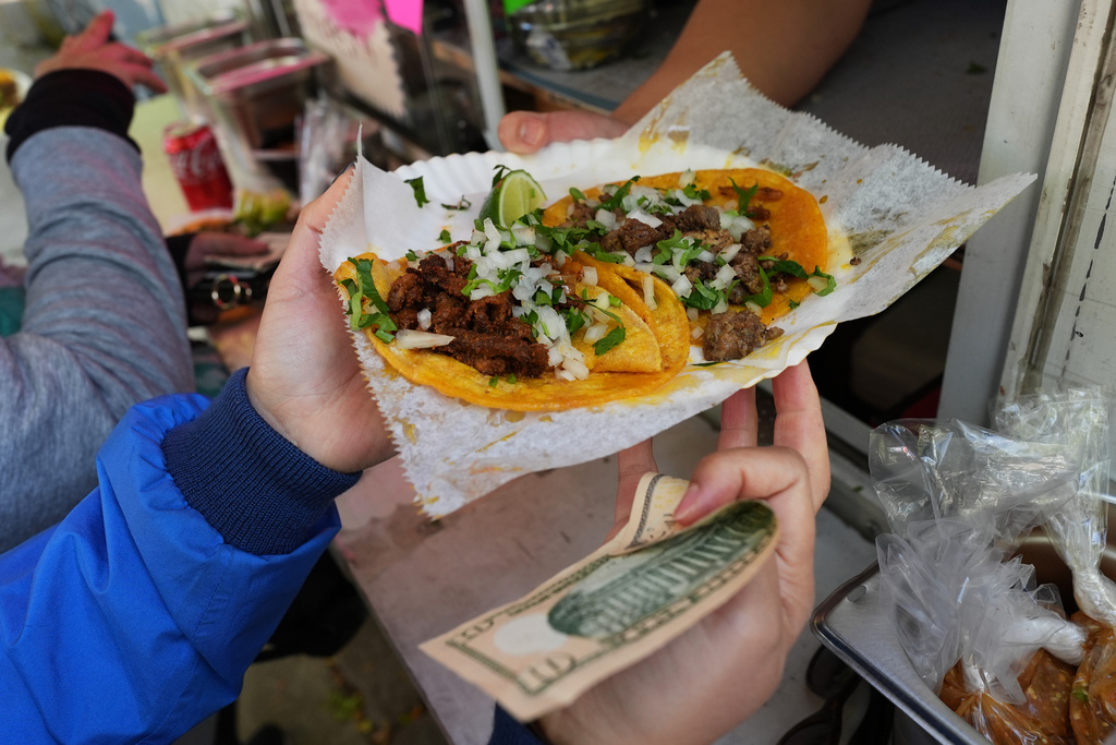 Bicyclist receives food from a street vendor Yulisa Robles at Gage Park during Street Vendor Bike Tour Series, in Chicago