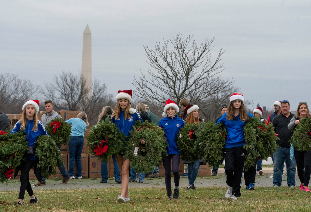 Volunteers walk with holiday wreaths to lay at headstones in Arlington National Cemetery during Wreaths Across America Day 