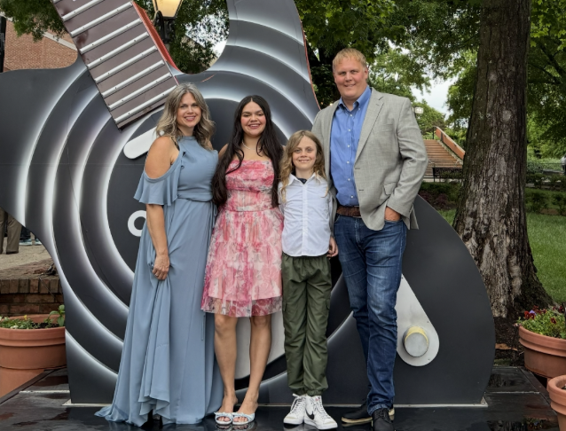 Man with wife and two kids in front of a large guitar