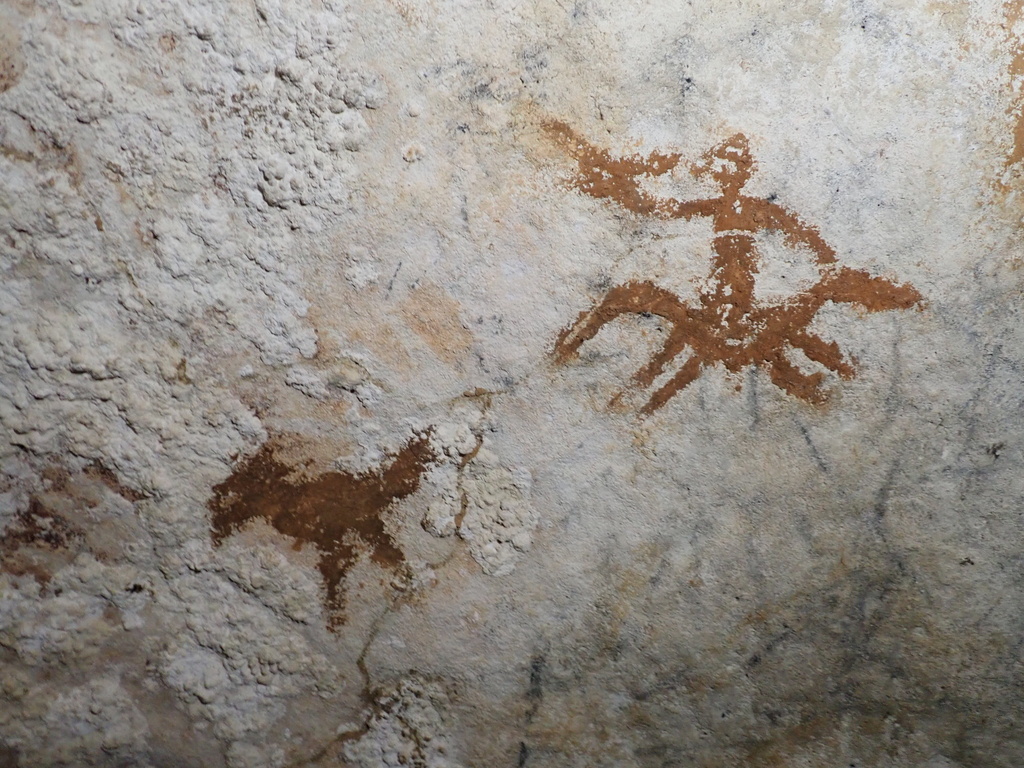 cave drawings in Sulawesi, Indonesia of a human figure and a bird with a faded handprint in between them