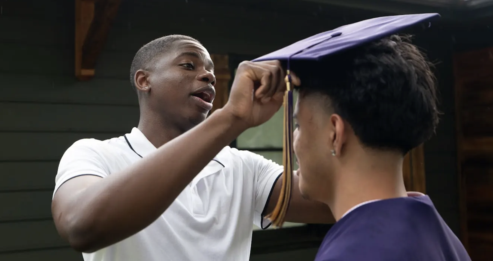 Older young man helps younger man with his graduation cap
