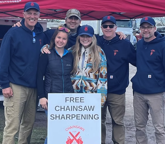 Group of people near a red tent and a sign that says "Free Chainsaw Shapening"