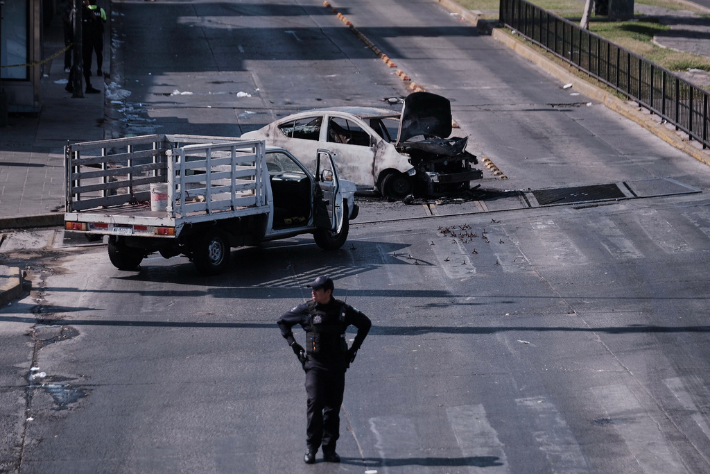 A police officer stands guard by a charred vehicle after it was set on fire, on a road in Guadalajara, Jalisco 