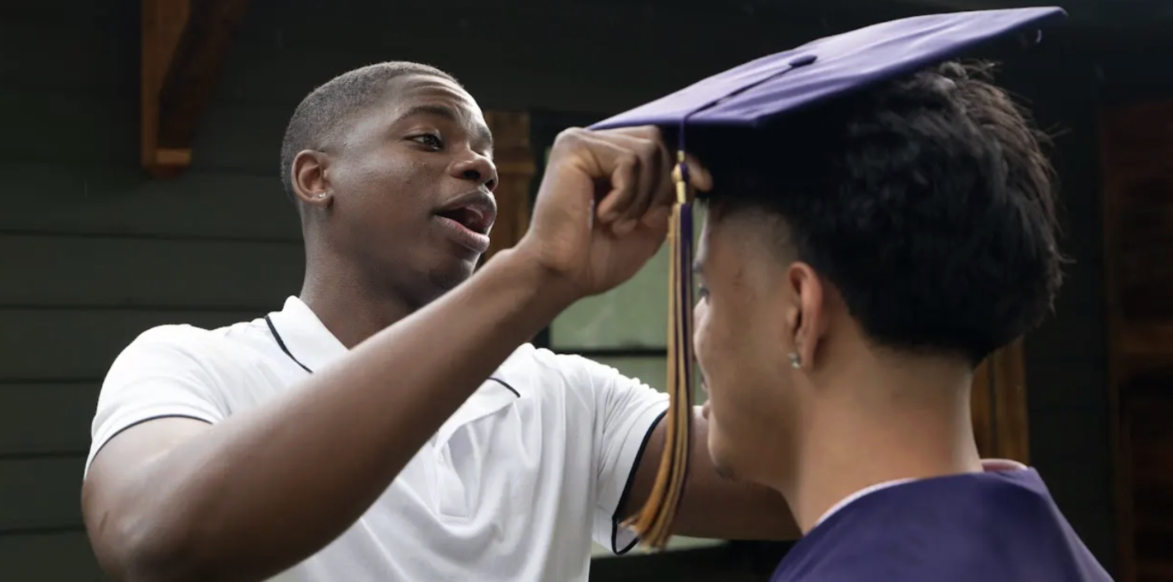Young man putting graduation cap on another young man