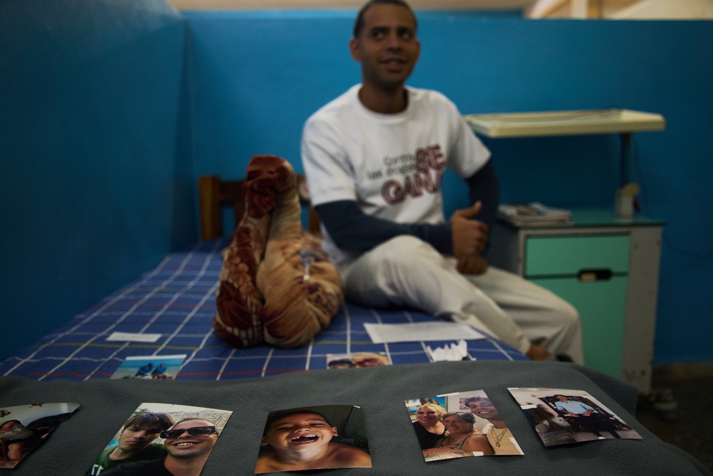 A youth in rehabilitation sits on his bed next to photos of his family that he uses as support for his recovery at a psychiatric hospital in Havana