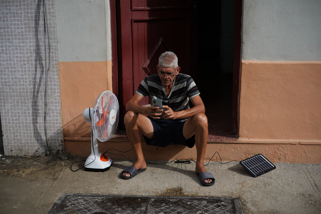 A man charges his phone and his fan with a solar panel during a blackout in Havana