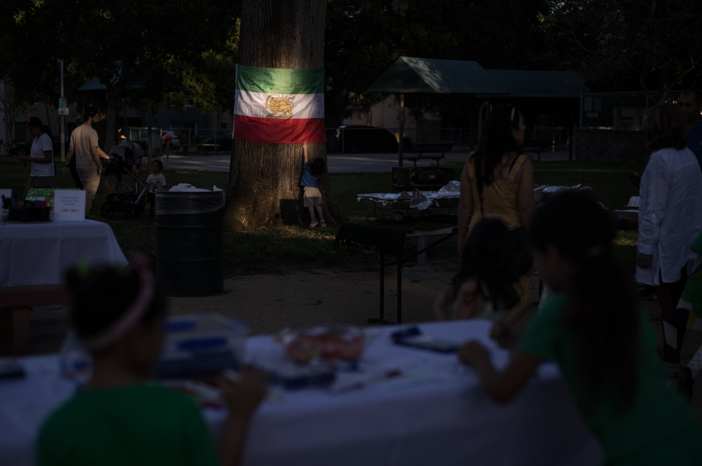 A young boy touches an Iranian flag lit by afternoon sunlight during a community gathering ahead of the Nowruz holiday in the Encino neighborhood of Los Angeles
