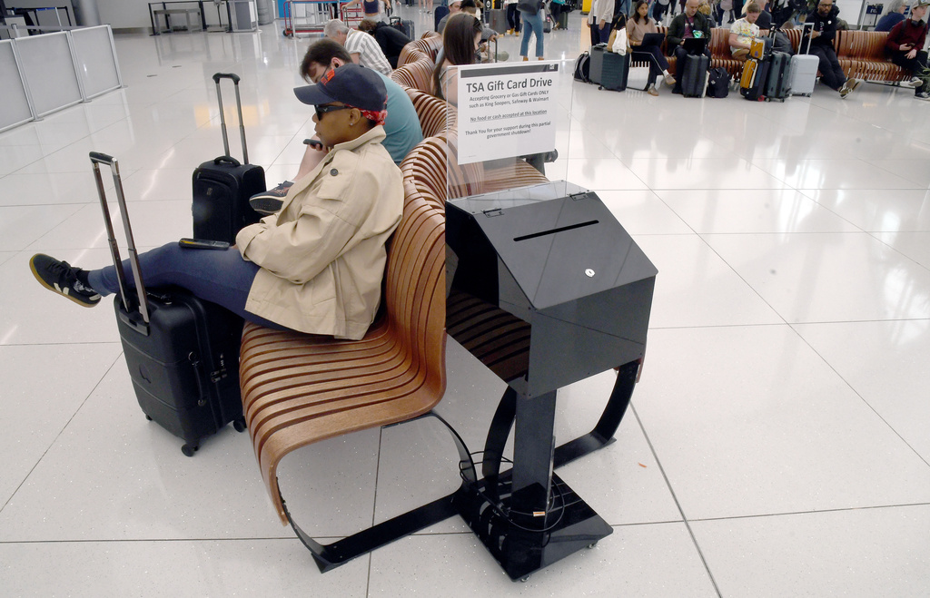 Travelers sit near a gift card donation box for Transportation Security Administration officers at Denver International Airport 