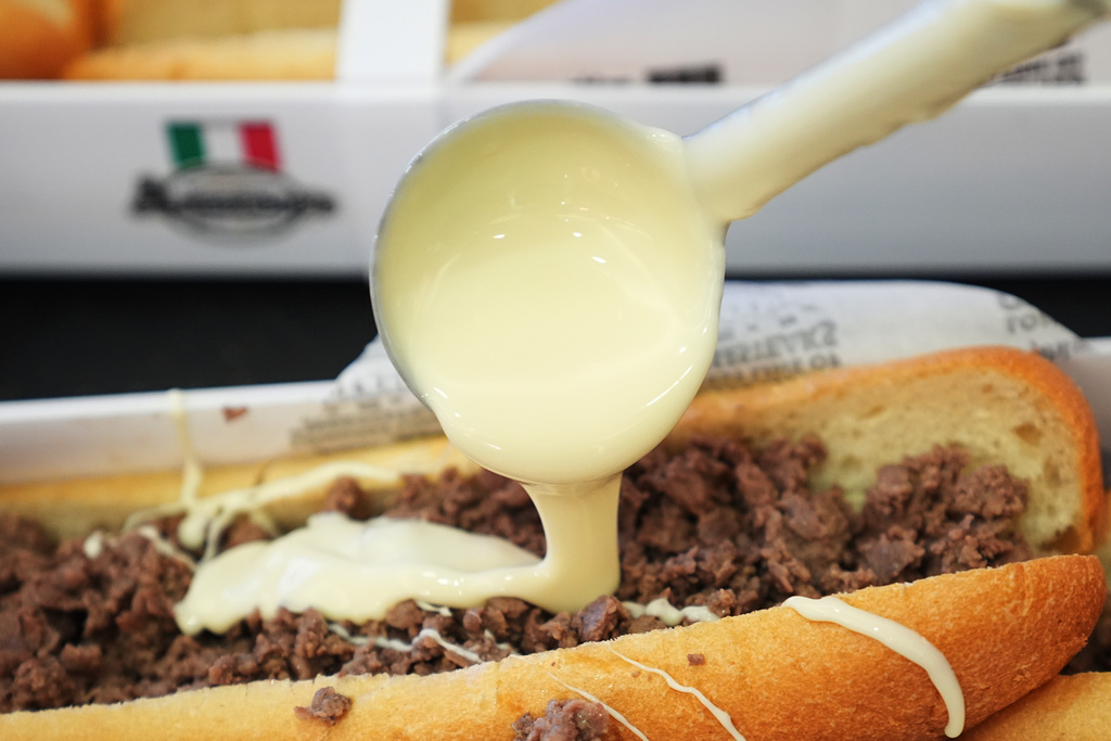 A volunteer ladles out cheese onto one of many cheesesteaks as part of a Guinness World Record attempt 