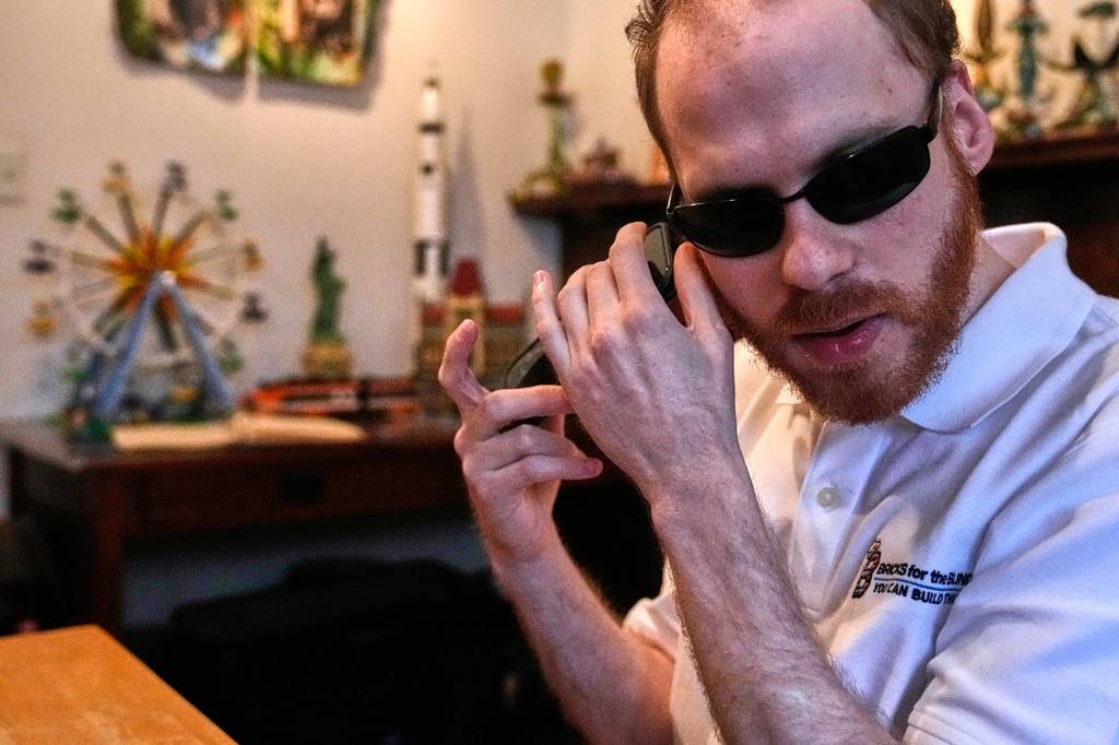 Matthew Shifrin, the founder of Bricks for the Blind, listens to directions on his phone while building a LEGO gum ball machine 
