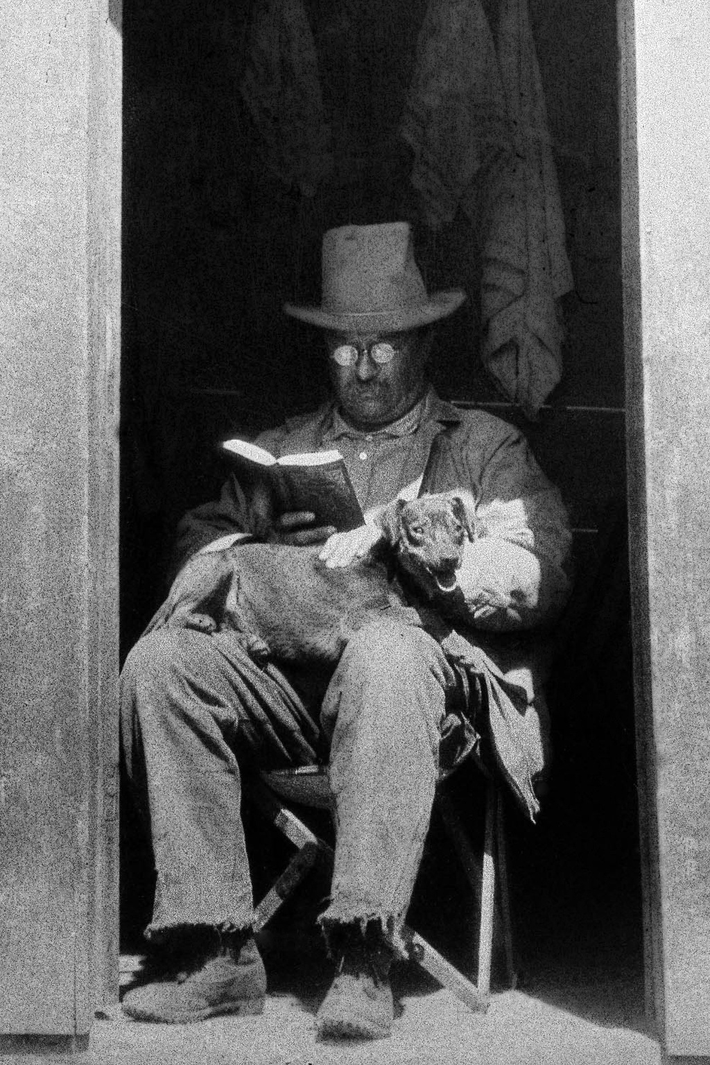 President Theodore Roosevelt reads a book with his dog skip on his lap, in the doorway of the West Divide Creek ranch house in Meeker, Colo.