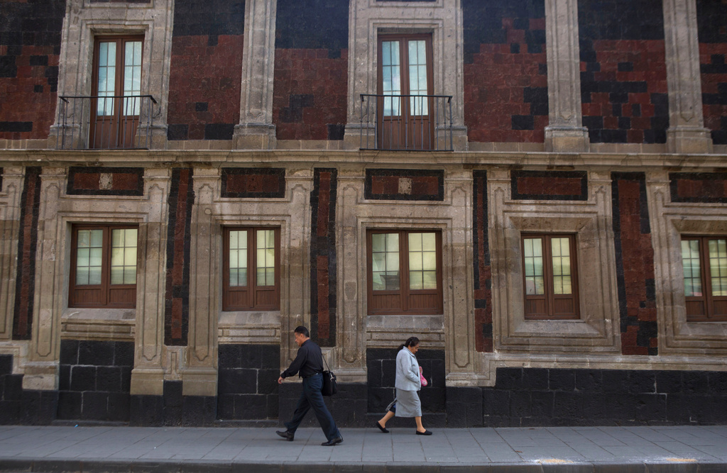 Pedestrians walk past a slightly tilted historic building in downtown Mexico City