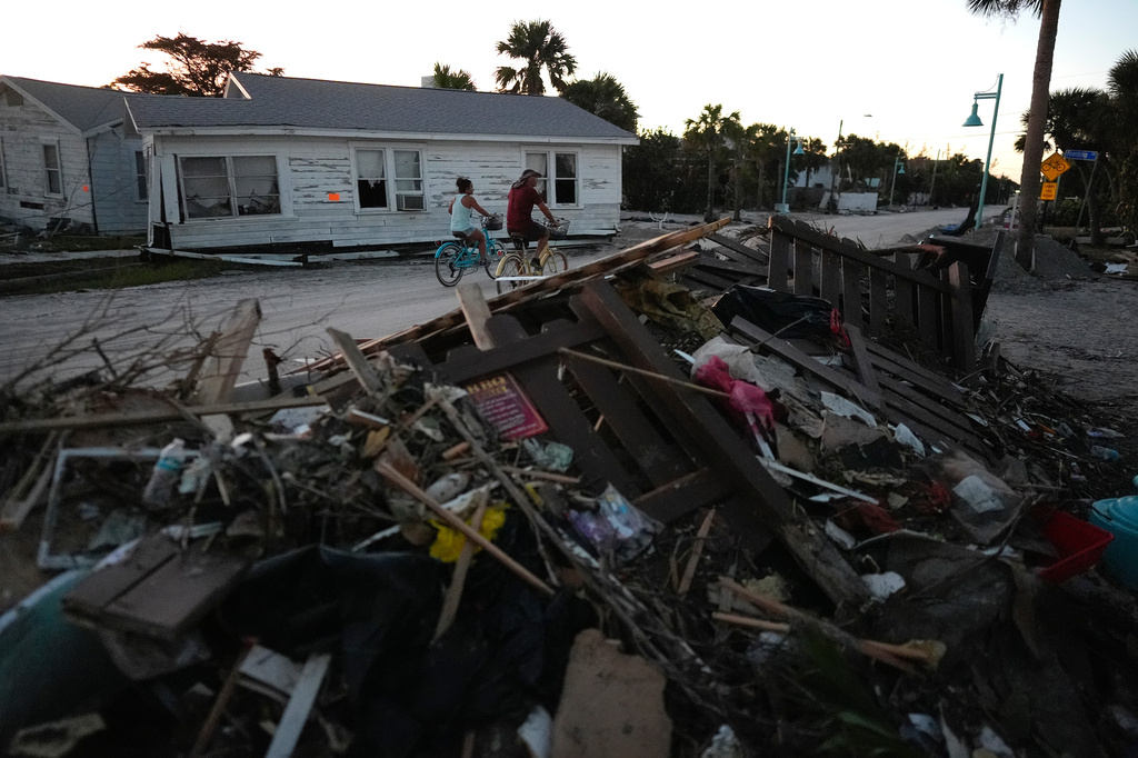 People bike past damaged homes and debris left by Hurricane Milton, on the sand-coated main road of southern Manasota Key, already cleared of feet of sand, in Englewood, Fla., Oct. 13, 2024.