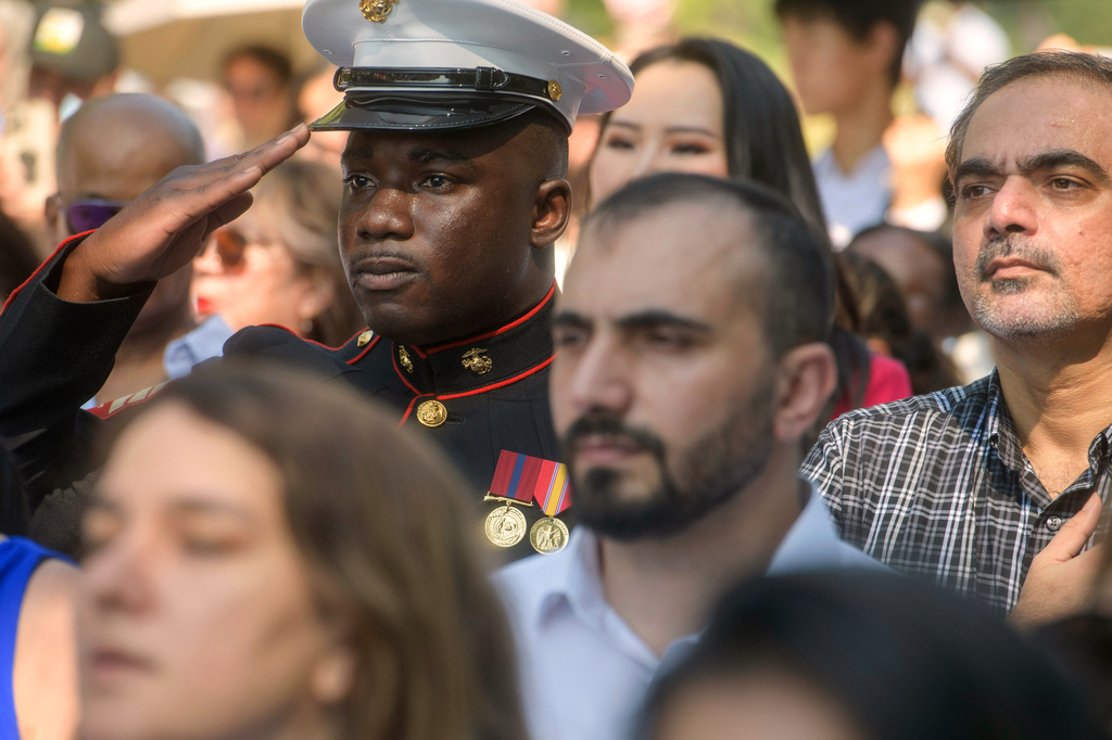 U.S. Marine Sgt. Diakaria Sangare, center, from Guinea, salutes the playing of the national anthem at a naturalization ceremony on Independence Day