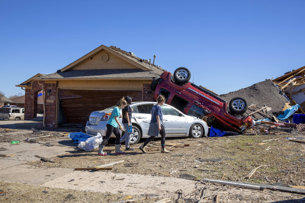 Neighbors walk in front of a home damaged in Norman, Okla.