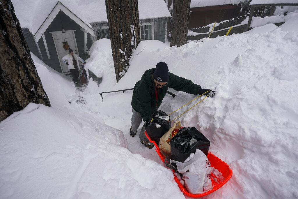 Angie Gourirand walks down the snow-covered steps of her home with groceries on a sled in Running Springs, Calif.