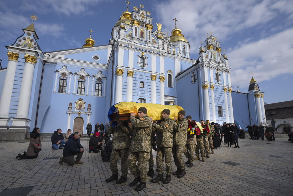 People kneel as servicemen carry a coffin of a Ukrainian serviceman Oleksiy Sokolovskyi during the funeral ceremony in St. Michael Cathedral in Kyiv