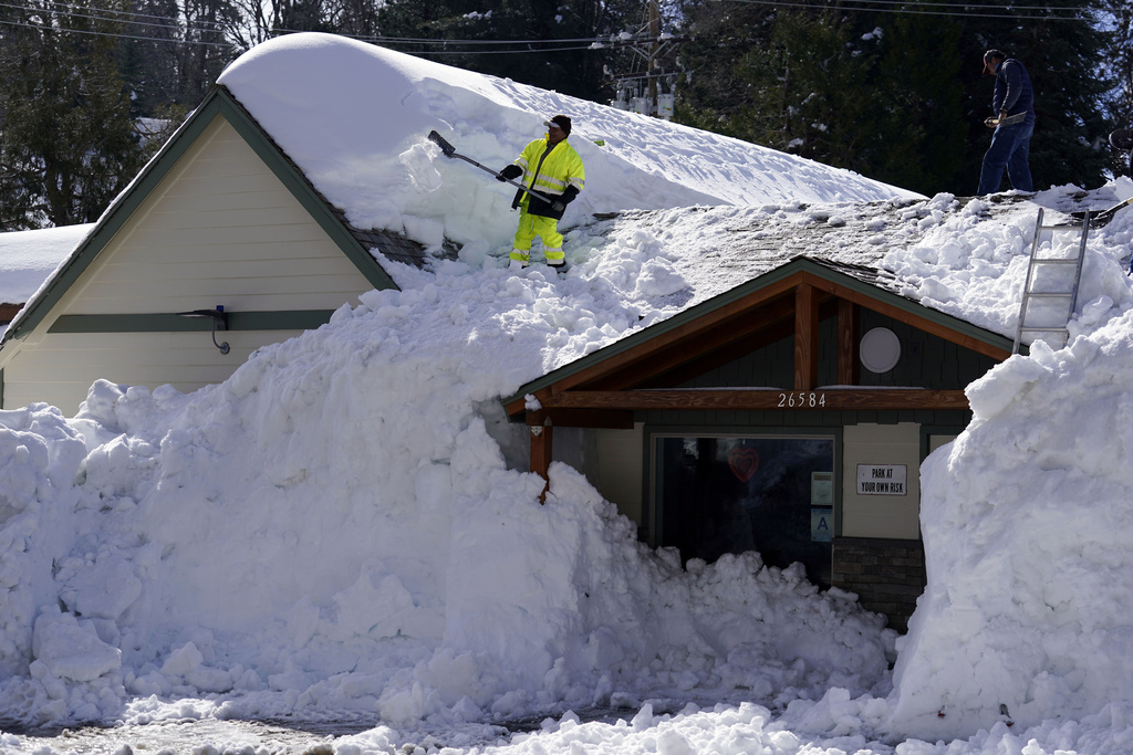 A worker clears snow off the roof of Skyforest Elks Lodge after a series of storms in Rimforest, Calif. 