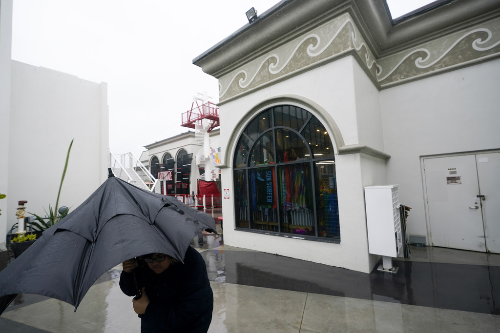 A woman walks under an umbrella at a vacant Belmont Park as rain engulfs the area in San Diego