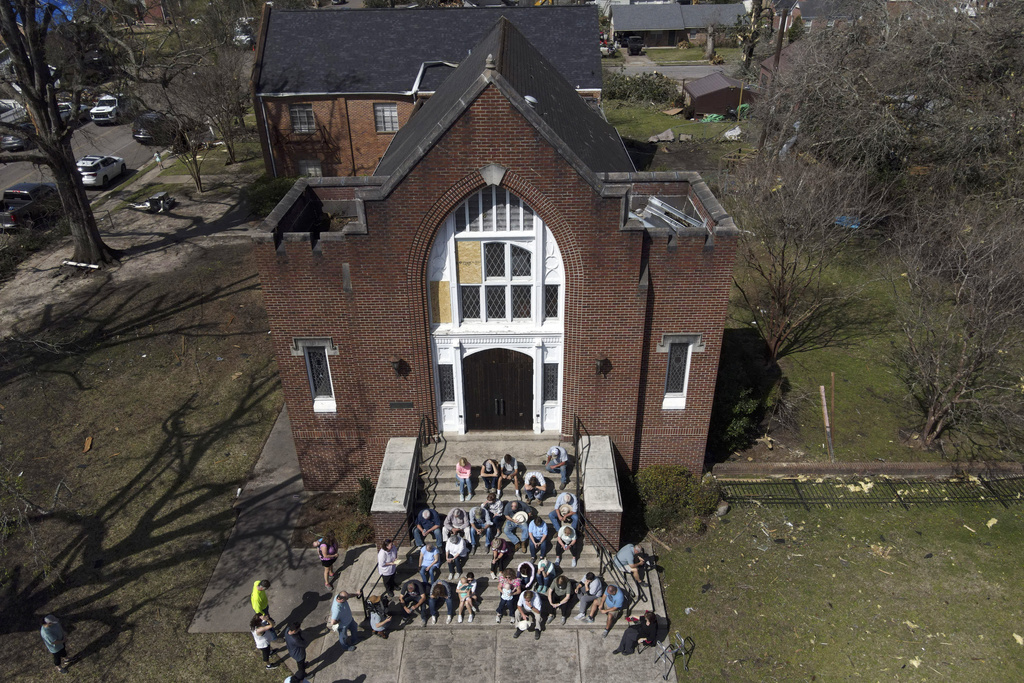 People worship on the steps of the Rolling Fork United Methodist Church, right, as damage is visible to surrounding properties