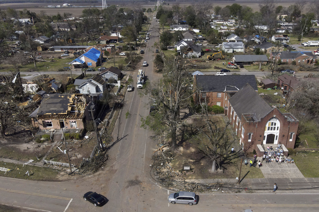 People worship on the steps of the Rolling Fork United Methodist Church, right, as damage is visible to surrounding properties