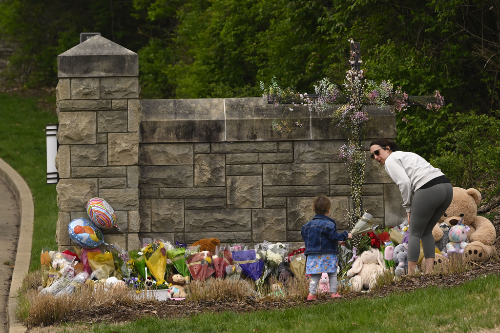 A woman and child bring flowers to lay at the entry to Covenant School