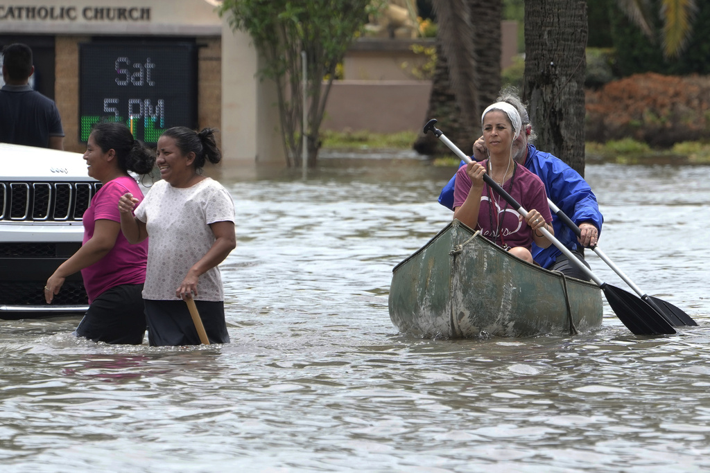 Residents paddle and walk along a flooded road in Fort Lauderdale, Fla.