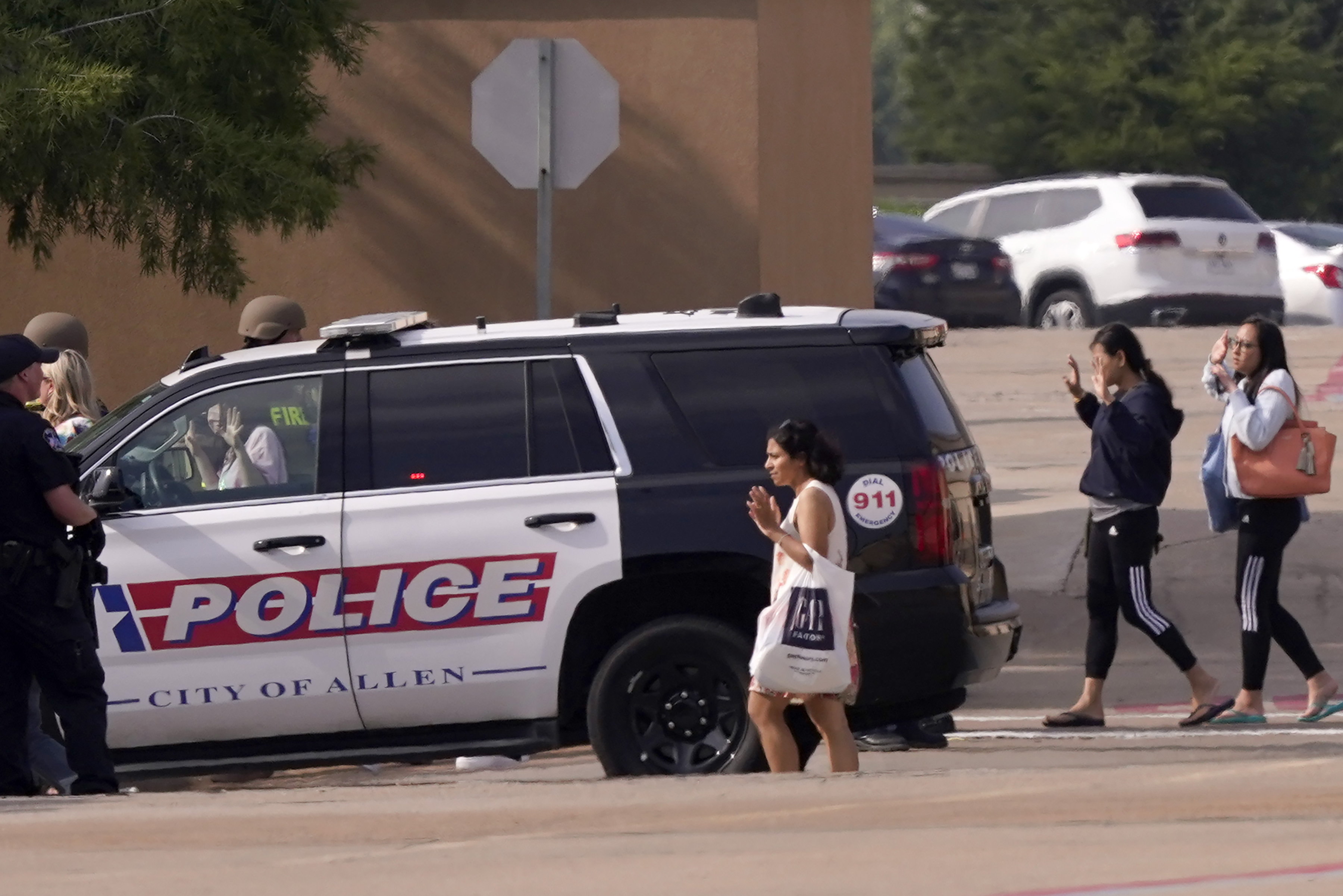 People raise their hands as they leave a shopping center after a shooting, Saturday, May 6, 2023, in Allen, Texas.